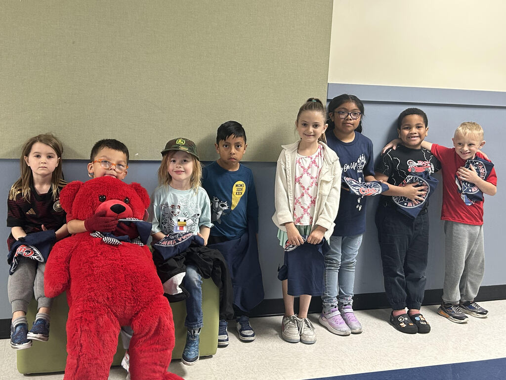 Group of smiling children holding YV cub t-shirts and one boy holding a big read stuffed bear.