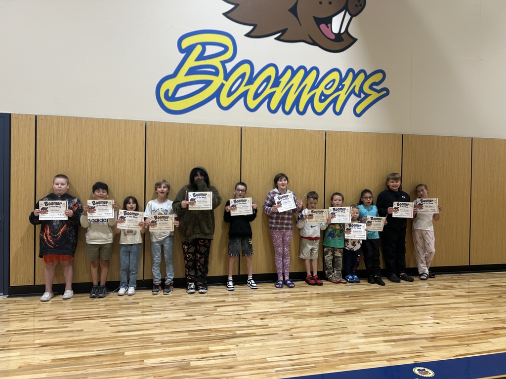 Group photo of elementary students holding certificates in gym under Boomers logo and mascot