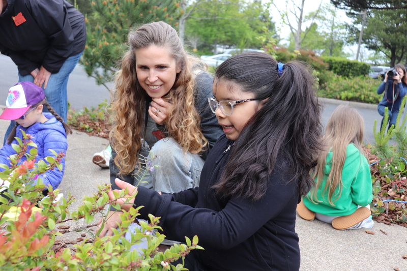 girl in black shirt touches plant while women with blond hair looks on