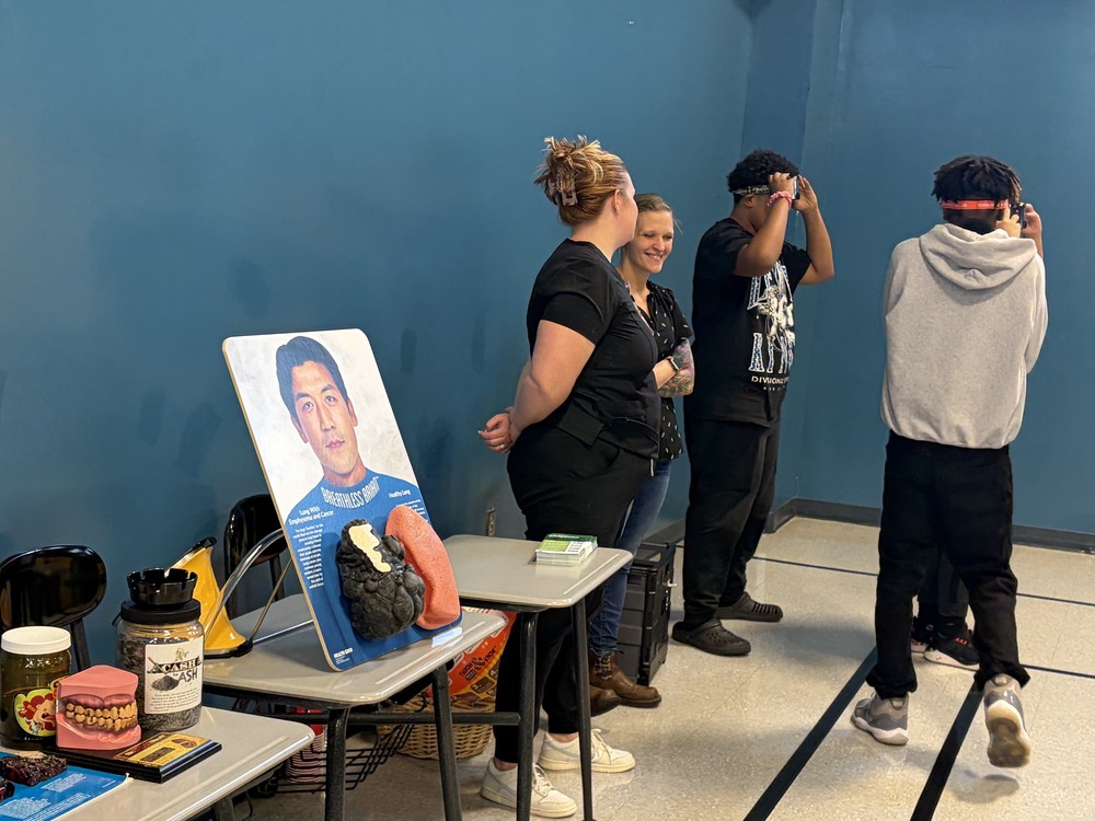 Students and instructors around an educational health display with VR headsets.