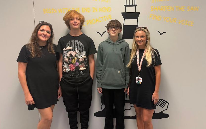 A photo of 2 guidance counselor and 2 students standing in front of a wall with a lighthouse.