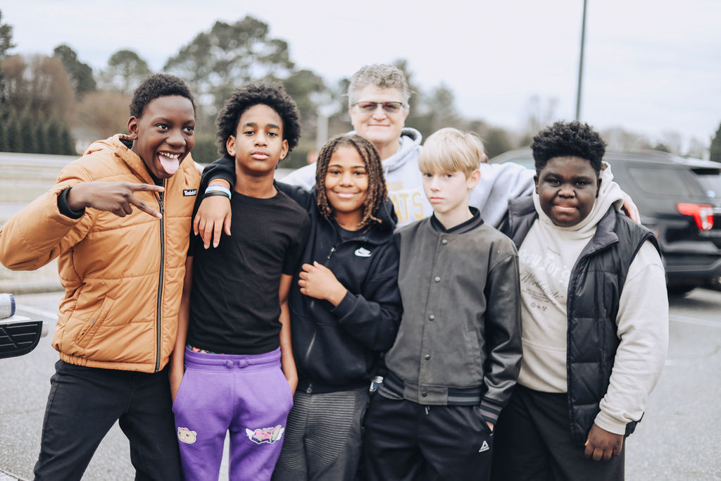 Six middle school students and an adult stand together in a parking lot, smiling and posing for a group photo after a hands-on activity.