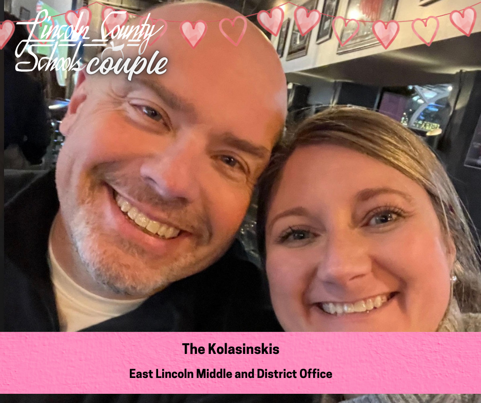 Close-up photo of a smiling couple taking a selfie indoors, with framed pictures visible on the wall behind them. A banner of pink hearts across the top reads “Lincoln County Schools couple.” A pink label at the bottom reads, “The Kolasinskis – East Lincoln Middle and District Office.”