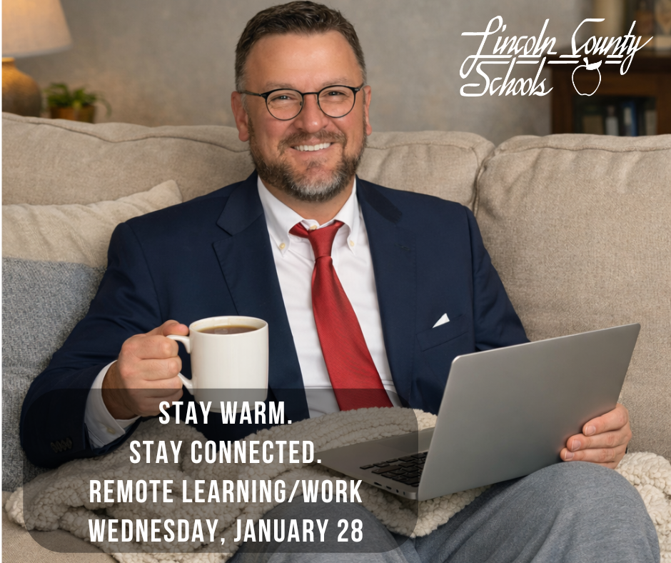 Superintendent sitting on a couch with a blanket over his lap, wearing a suit jacket and red tie with gray sweatpants, holding a mug of coffee in one hand and a laptop in the other, smiling at the camera. Text on the image reads, “Stay warm. Stay connected. Remote learning/work Wednesday, January 28,” with the Lincoln County Schools logo in the top right corner.