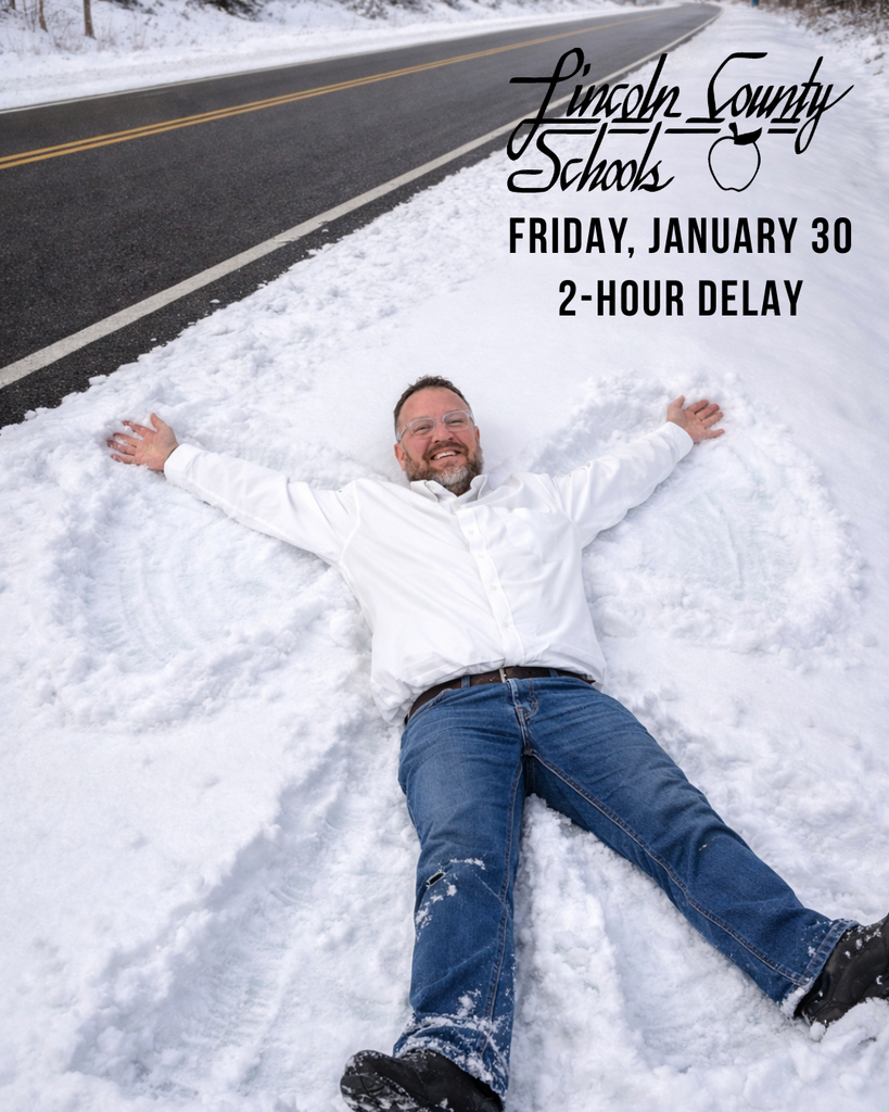 A smiling adult man wearing a white button-down shirt, jeans, and boots lies on his back in the snow beside a clear, dry roadway, arms and legs spread as if making a snow angel. Snowbanks line the road, and trees are visible in the background. Text in the upper right reads, “Lincoln County Schools. Friday, January 30. 2-Hour Delay.”