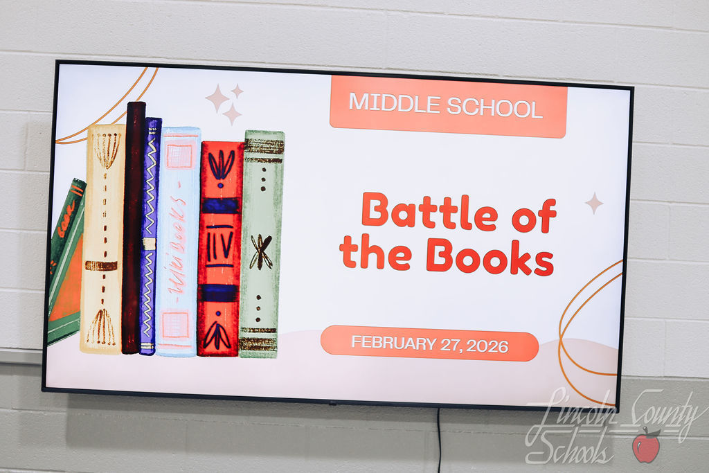 A digital display screen reads “Middle School Battle of the Books – February 27, 2026” with an illustration of stacked books on the left side.