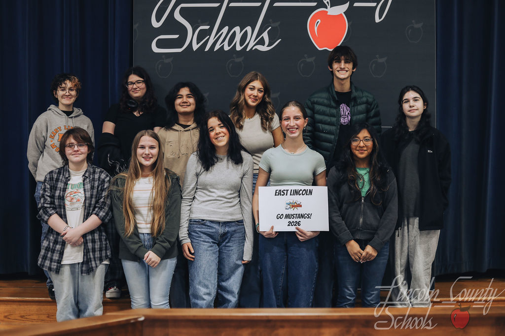 Group of East Lincoln High School students posing on stage in front of a Lincoln County Schools backdrop. One student holds a sign reading “East Lincoln – Go Mustangs! – 2026.”
