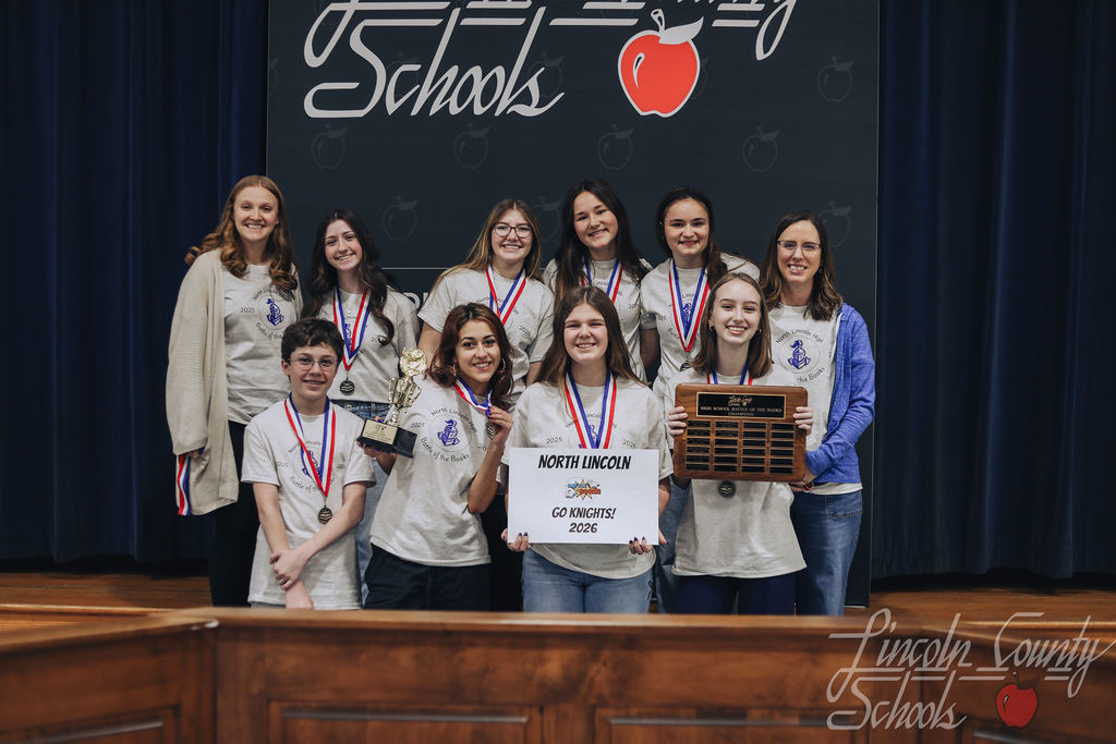 North Lincoln High School students and a coach pose on stage with medals. Students hold a trophy, a plaque, and a sign reading “North Lincoln – Go Knights! – 2026.”