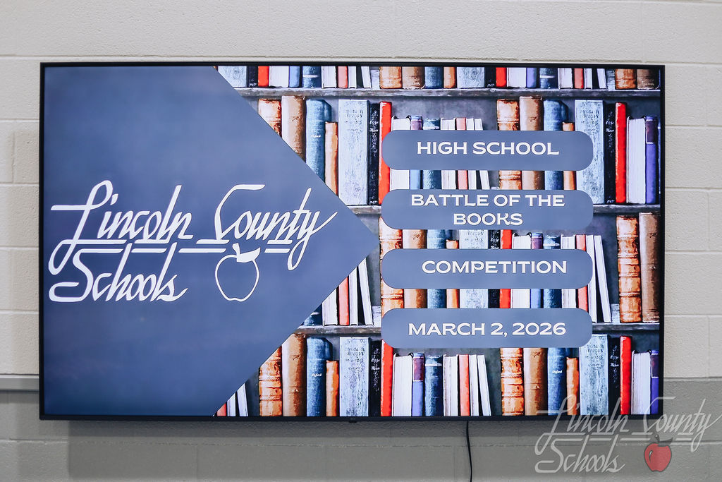 Digital display screen showing “Lincoln County Schools – High School Battle of the Books Competition – March 2, 2026” over a bookshelf background.