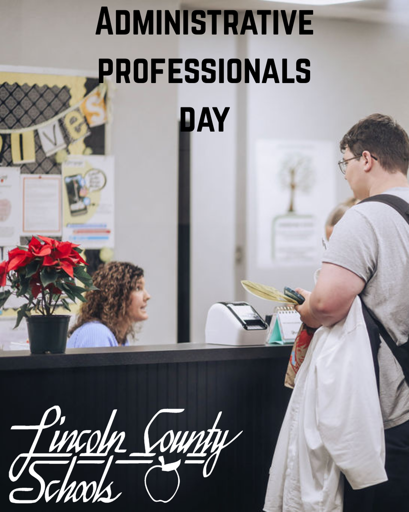 A school office scene where an administrative professional sits behind a front desk speaking with a visitor standing at the counter holding papers and a bag. A poinsettia plant sits on the desk, and school notices are posted on the wall behind them. Text at the top of the image reads “Administrative Professionals Day,” and the Lincoln County Schools logo appears at the bottom.