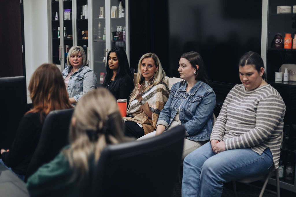 A small group of women, including students and professionals, sit in a circle during a discussion, listening as one woman speaks and gestures while sharing her experience.