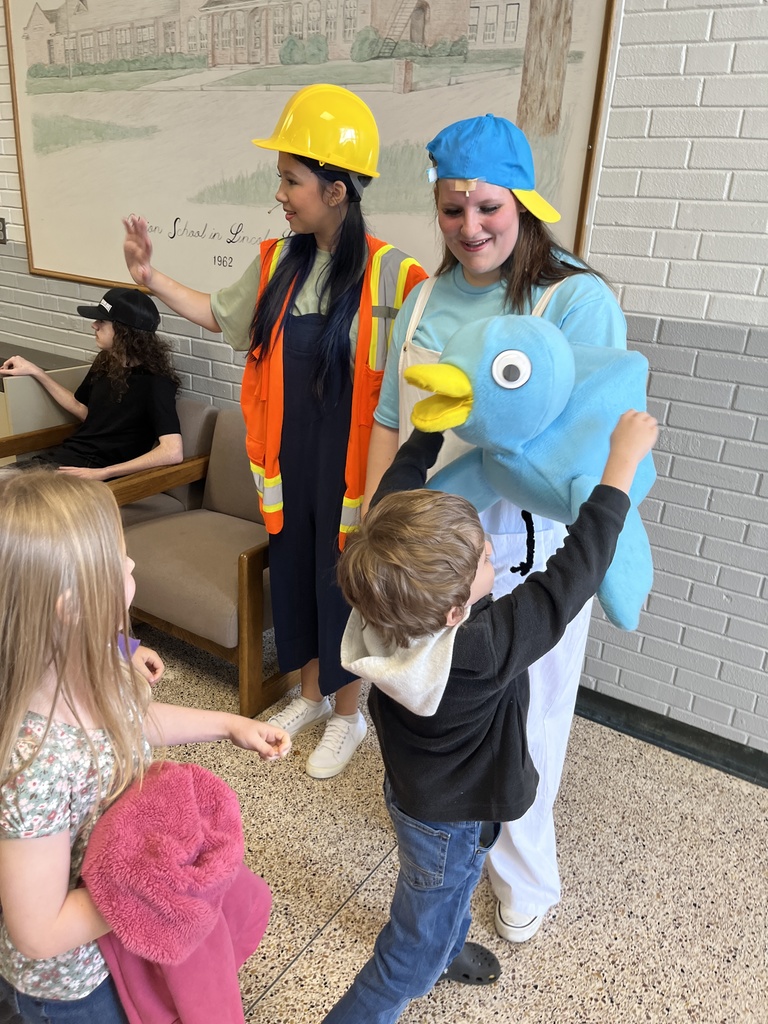 Two costumed actors—one holding the Pigeon puppet—interacting with an excited young child in the auditorium's lobby. The child has their arms open for a hug with the Pigeon puppet.