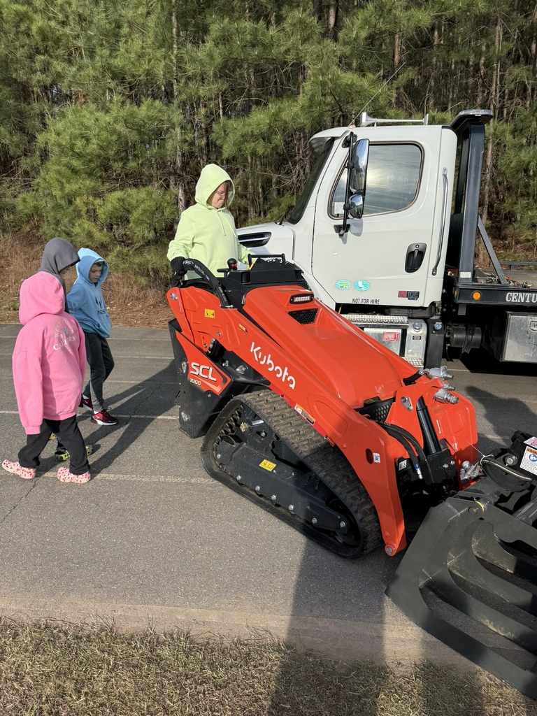 Three people stand near a red bulldozer, while a truck with a flatbed trailer is parked behind them.