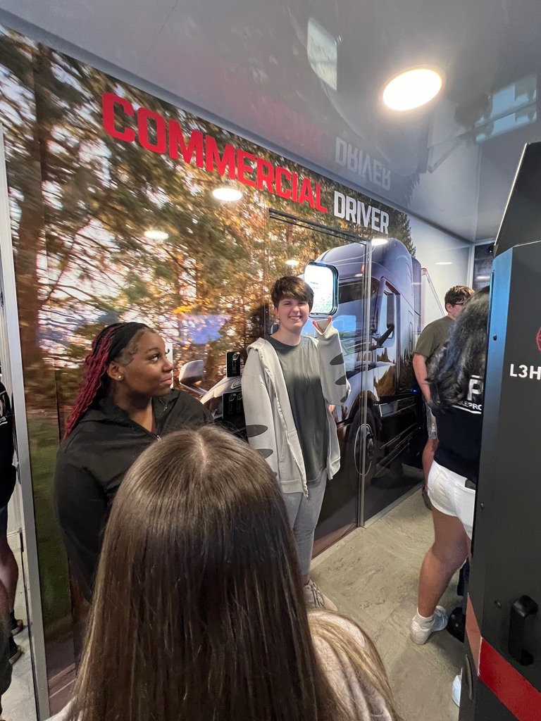 People stand in front of a large commercial truck display wall. A large truck image is on the wall.