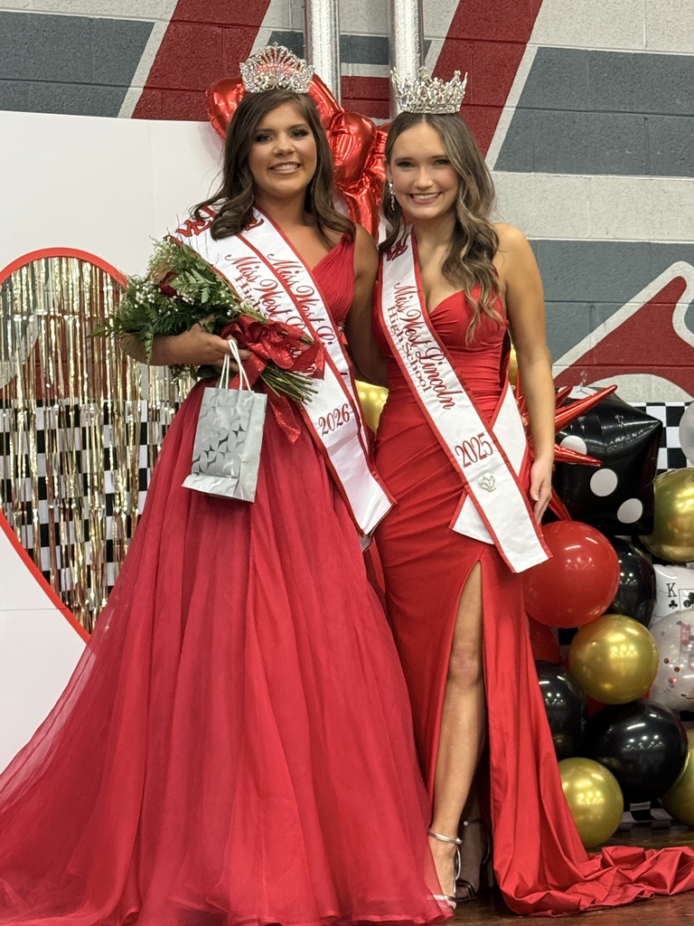 Two women in red gowns and sashes, holding bouquets and handbags, stand together in front of a wall with balloons.