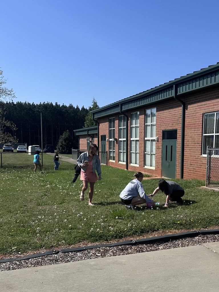 People outside a brick building, some standing and others sitting on the grass. One person crouches.