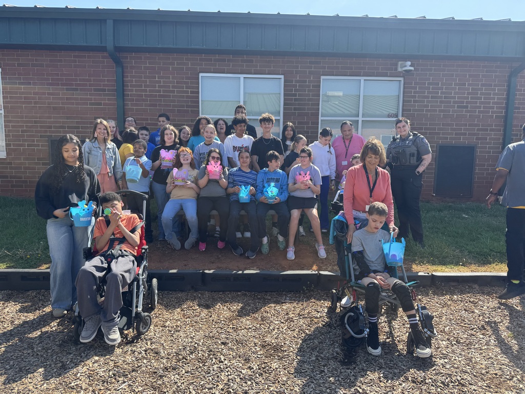 A group of people, including individuals in wheelchairs, are posing for a photo in front of a brick building.