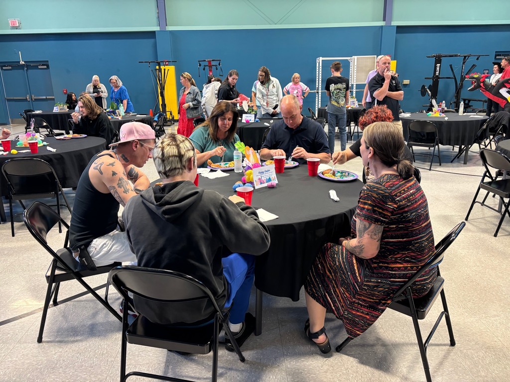People in a room with blue walls, sitting around round tables, some with plates and drinks.