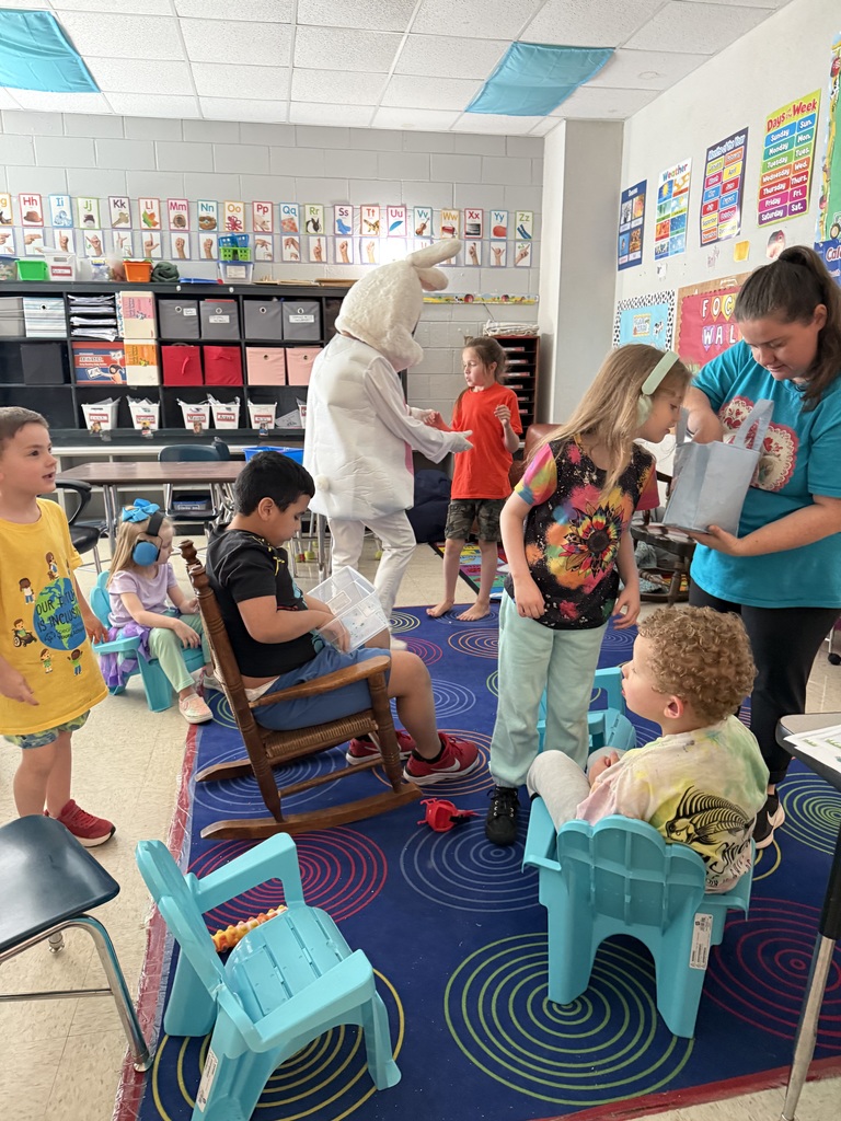A classroom with a teacher reading a book to students. The teacher is wearing a costume.