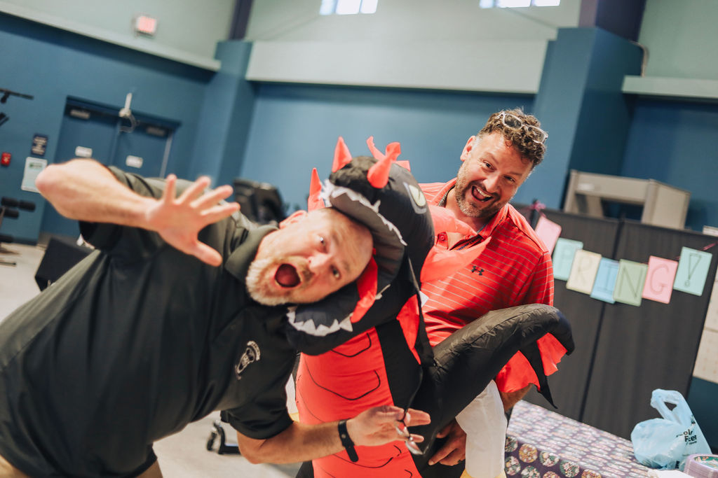 Two men in an indoor room. One wears a black dragon costume and the other a red shirt.