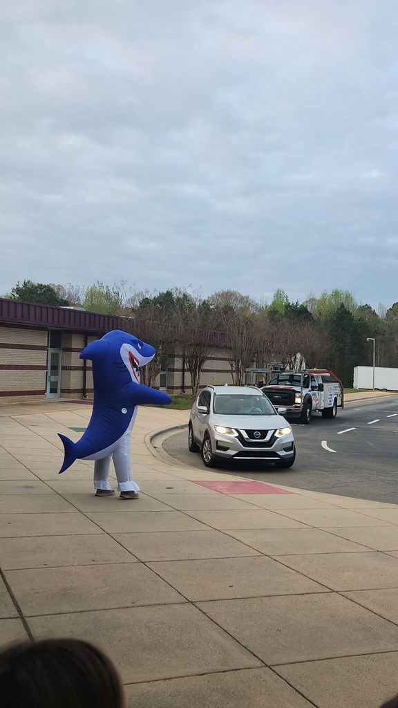 Man in shark costume greeting students at morning car line.