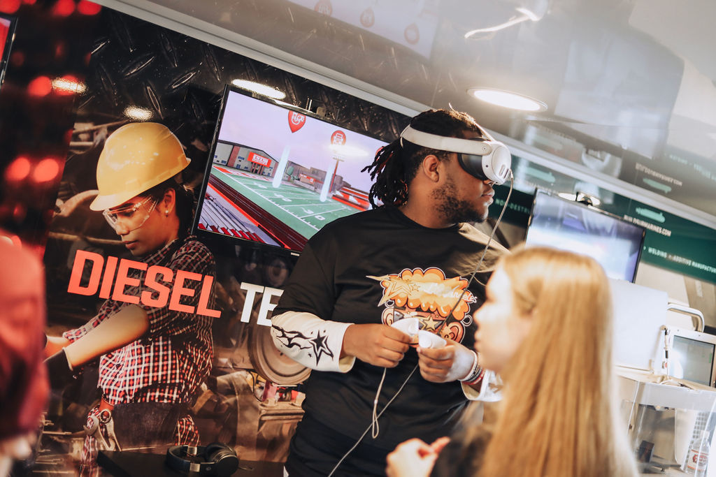People standing in front of a screen displaying a video game. One man holds a game controller.