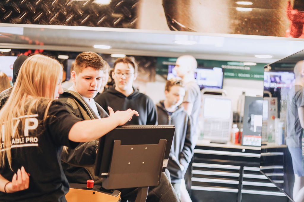 A group of people in a shop. A woman points at a computer screen while others watch.