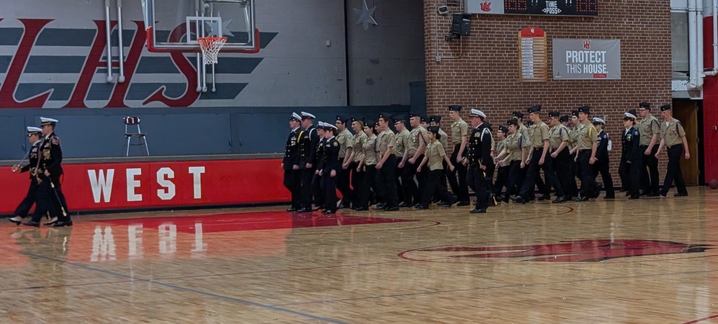 A group of people in uniform walk on a basketball court with "WEST" written in red.