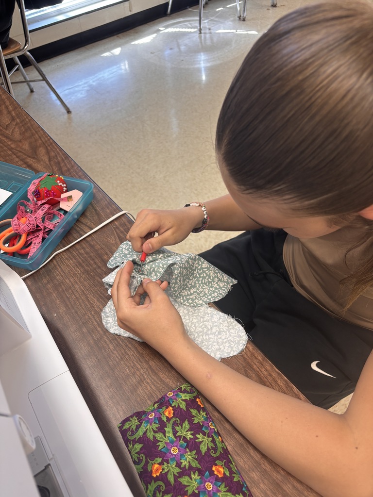 A person sits at a table, sewing fabric with scissors, with a colorful pouch on the table.