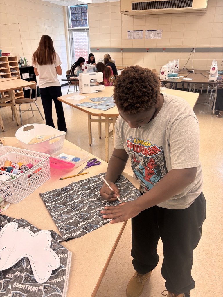 A person works at a table in a classroom. They draw on a piece of fabric.