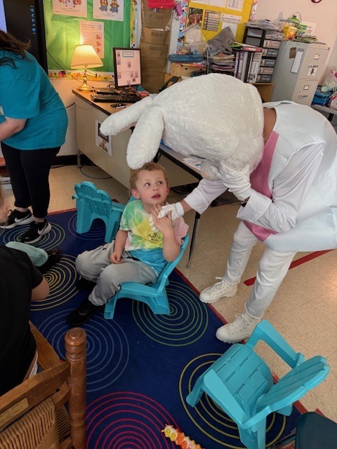 A person in a white costume sits with a child wearing a tie-dye shirt. They are indoors.