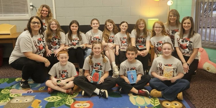 a group of students and teachers all smiling and holding books while sitting on a couch