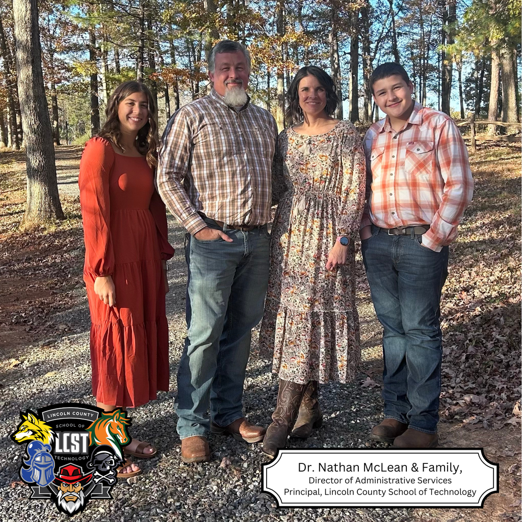 Four people pose on a gravel path in a wooded area. Three adults and a child.