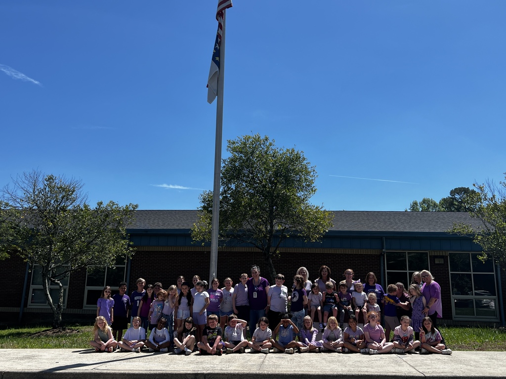 A large group of people wearing purple shirts poses for a photo in front of a school building.