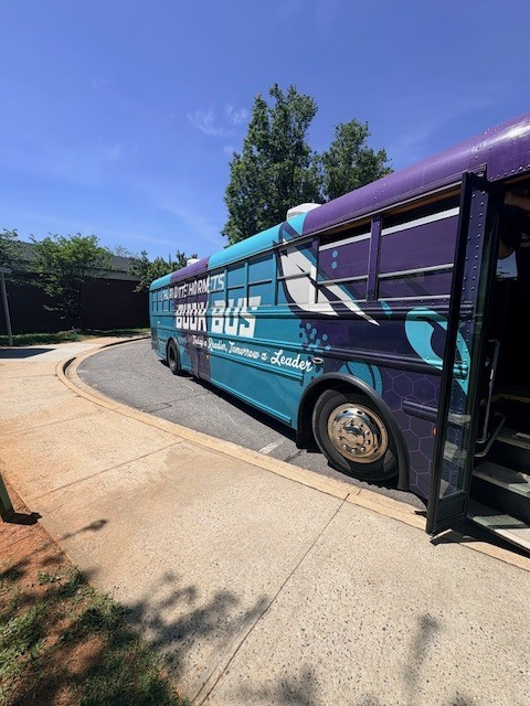 A blue and purple bus with the text "Sound Bus" is parked on a street. It has an open door.
