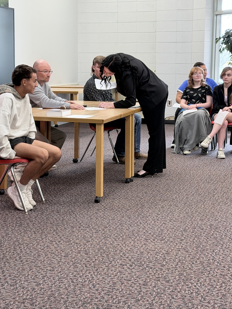 A person bends to sign a paper on a table while others sit around them.