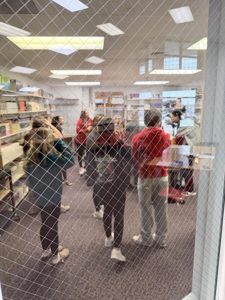 Blurred view through safety glass of a student in a red sweatshirt and grey sweatpants and other indistinct figures in an aisle. The safety glass wire mesh creates a textured pattern, obscuring clarity.