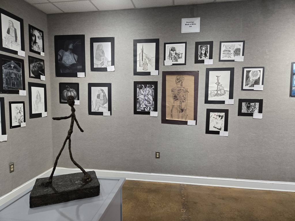 A wall of black and white ink drawings with a sculpture of a figure on a pedestal. 
