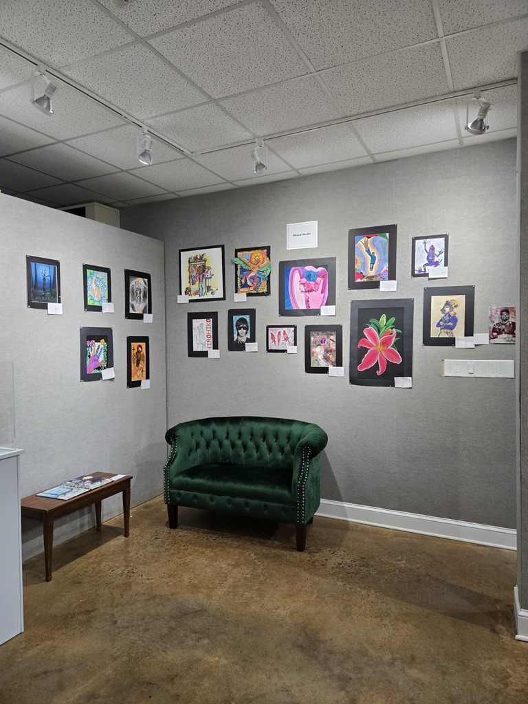 A wall of colorful mixed media artwork with a table and green couch. 