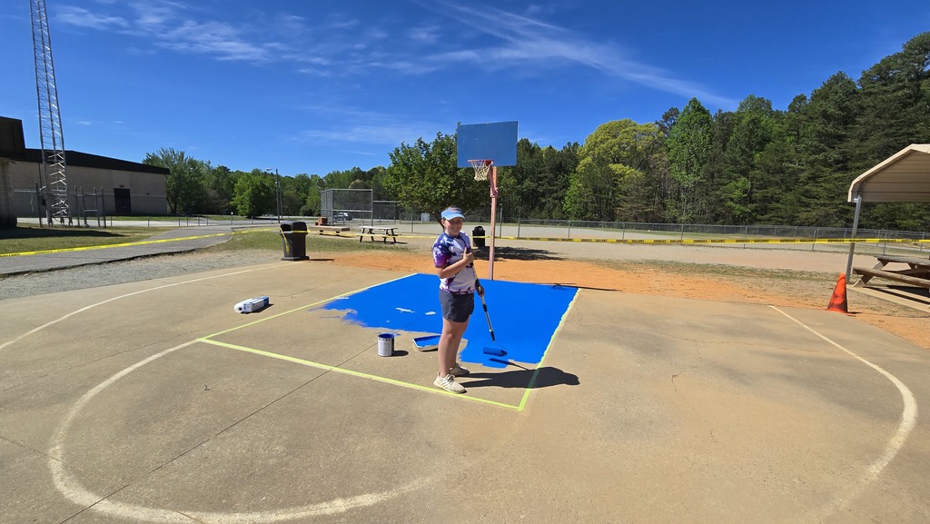 An individual in a hat, mask, and shorts standing on a basketball court, holding a golf club.