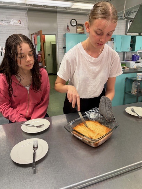 Two individuals, one in a white shirt and the other in a pink shirt, prepare food in a kitchen.