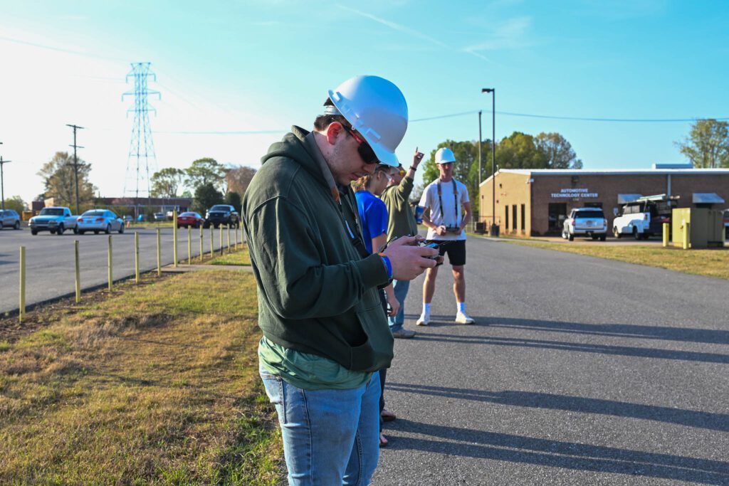 Students with white hard hats, directing their drones in the air.