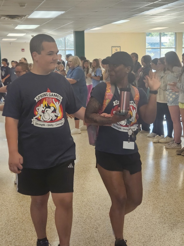 Two adults, one in a blue shirt, the other in a black shirt, walk toward a crowd.