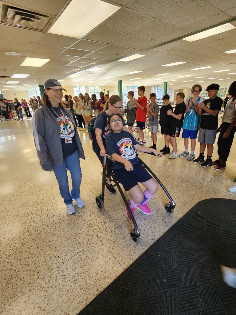 A person in a wheelchair is being pushed by another person through a hallway, surrounded by students.