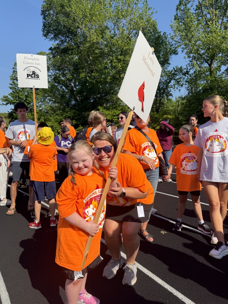 Group of people wearing orange shirts walk in a parade with signs. Some hold signs, while others follow.