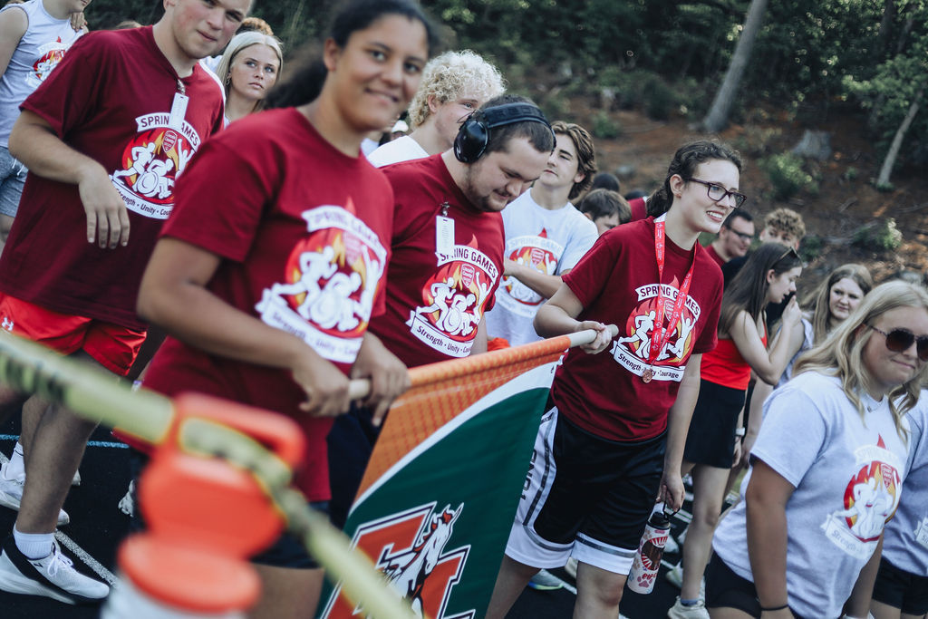 Group of individuals in red t-shirts with white graphics, one holding a flag, standing on a path.