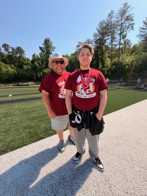Two people in red shirts, one wearing a hat, stand on a path near a field.