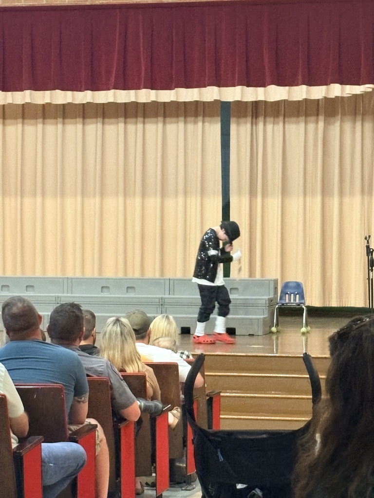 A person in black and white attire performs on stage before a seated audience in a theater.