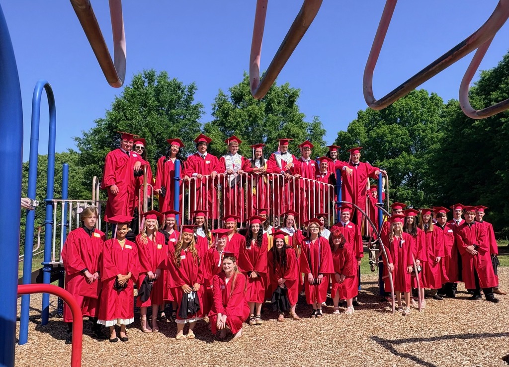 A group of people in red graduation gowns and hats poses for a photo in a playground.