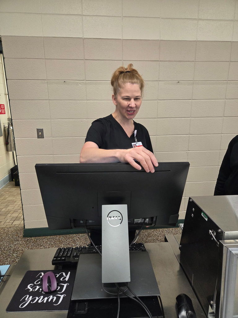 Person leaning over a monitor in the cafeteria. Monitor is on a table with a keyboard.